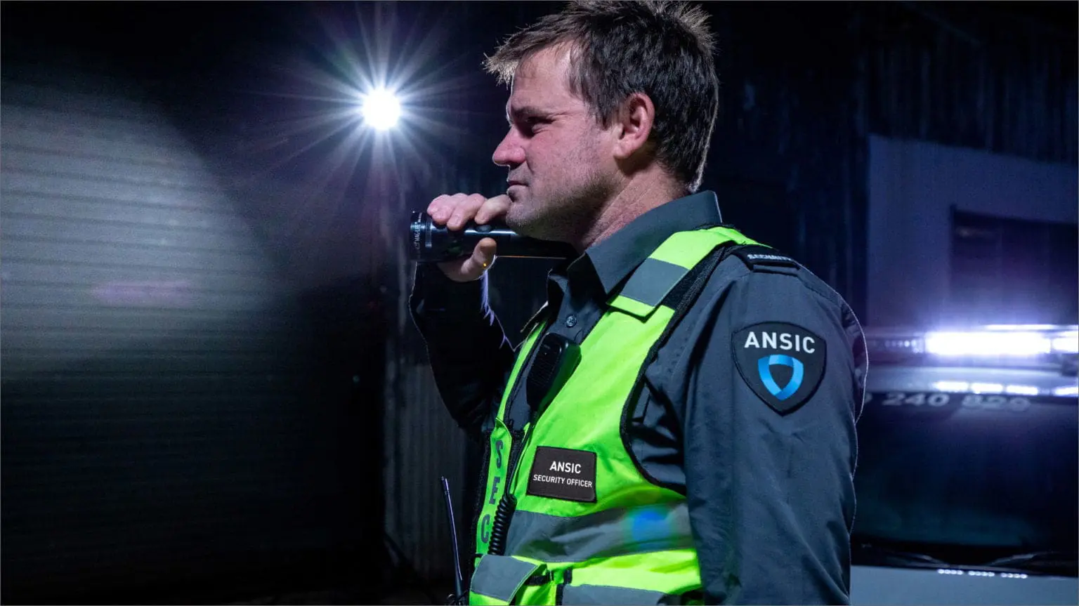 ANSIC security officer on night patrol beside a marked response vehicle