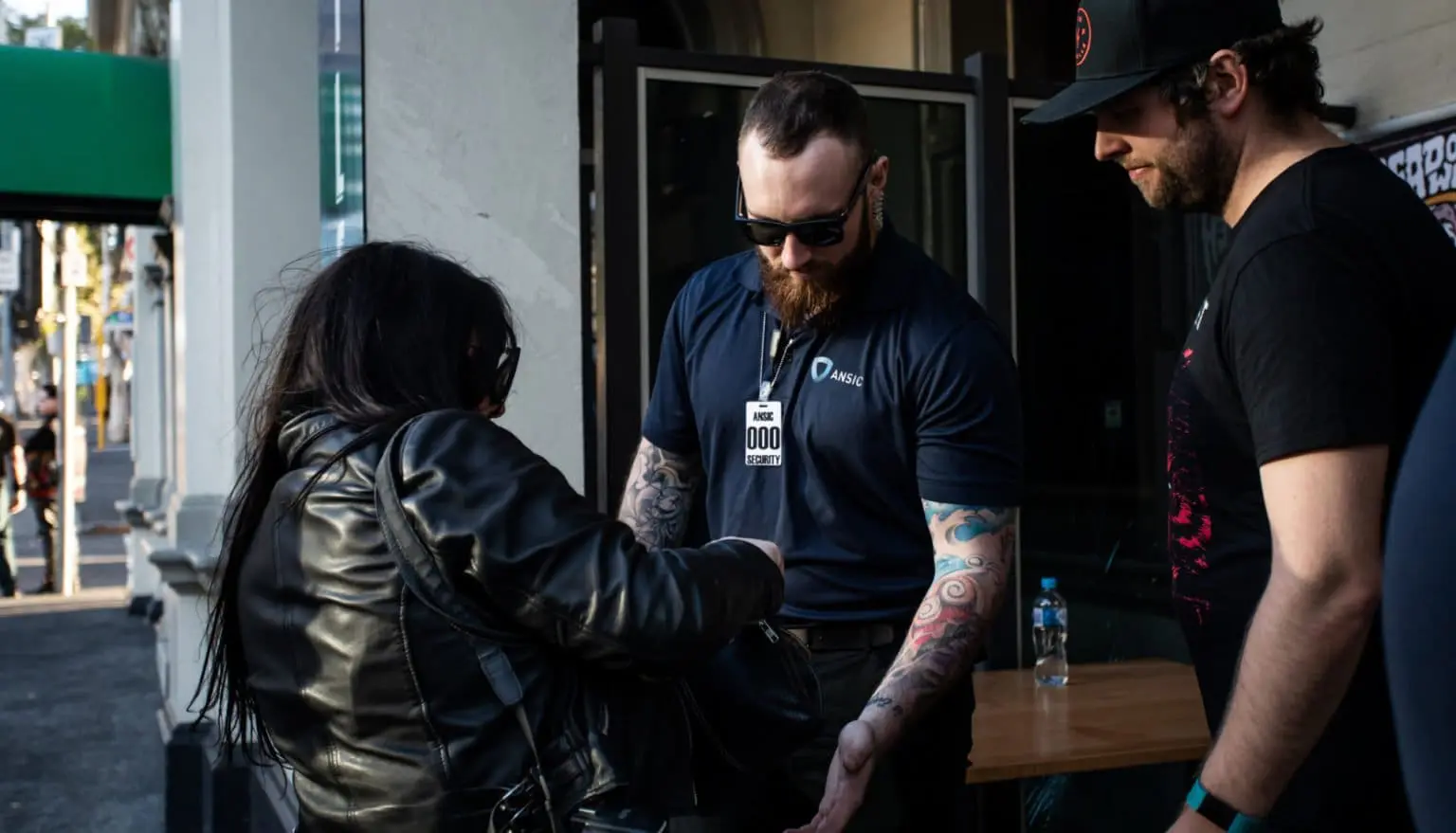 ANSIC security officer in a branded polo conducting a bag check at a venue entrance